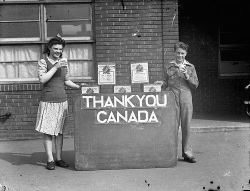 A young boy and girl standing, holding milk, standing next to a stand that says "Thank you Canada"