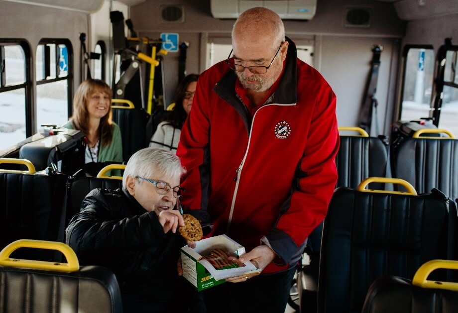 Man in Kin Canada jacket giving an oldaer woman in glasses cookies